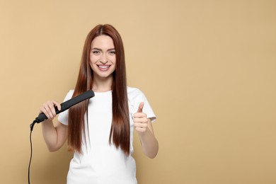 Beautiful woman using hair iron and showing thumbs up on beige background, space for text