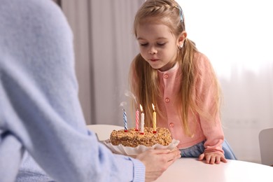 Photo of Birthday celebration. Mother holding tasty cake with burning candles near her daughter indoors