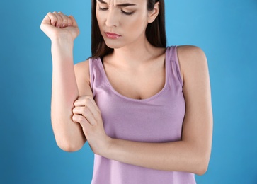 Photo of Young woman scratching hand on color background. Allergies symptoms