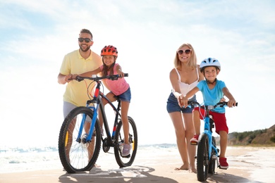 Photo of Happy parents teaching children to ride bicycles on sandy beach near sea