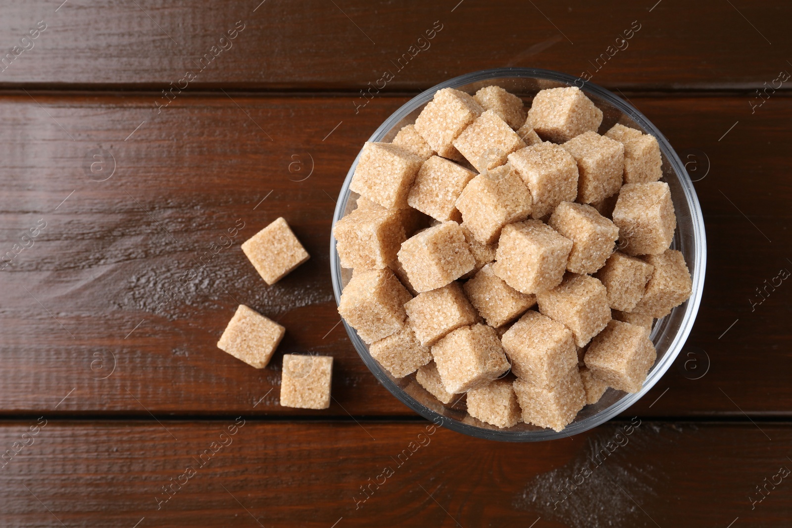 Photo of Brown sugar cubes in glass bowl on wooden table, top view. Space for text