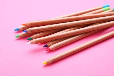 Photo of Many colorful pastel pencils on pink background, closeup. Drawing supplies