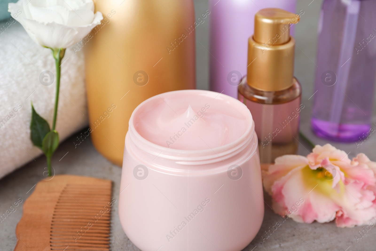 Photo of Different hair products, flower and wooden comb on grey table, closeup