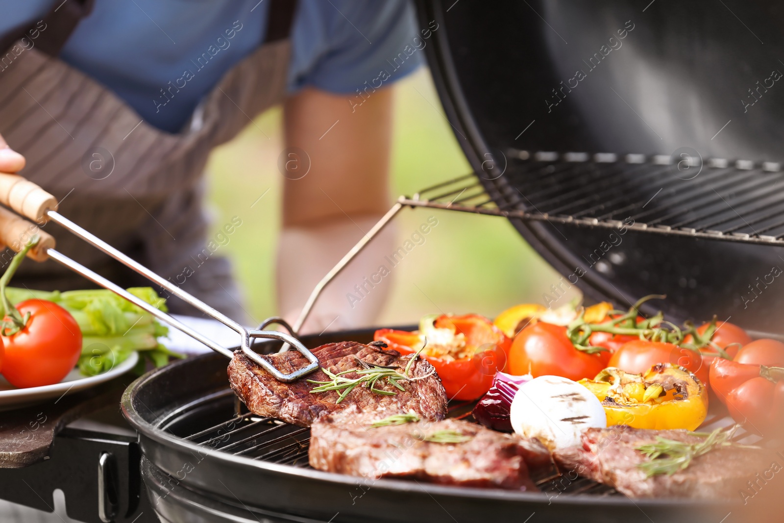 Photo of Man cooking meat and vegetables on barbecue grill outdoors