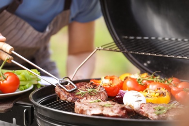 Man cooking meat and vegetables on barbecue grill outdoors