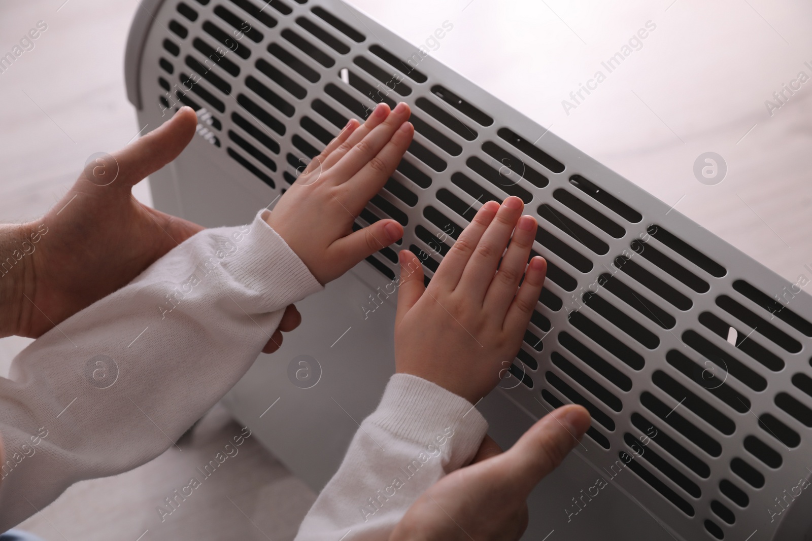 Photo of Father and child warming hands near electric heater at home, closeup