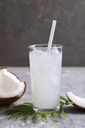 Photo of Glass of coconut water with ice cubes, palm leaf and nut on grey table