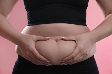 Photo of Woman touching belly fat on pink background, closeup. Overweight problem