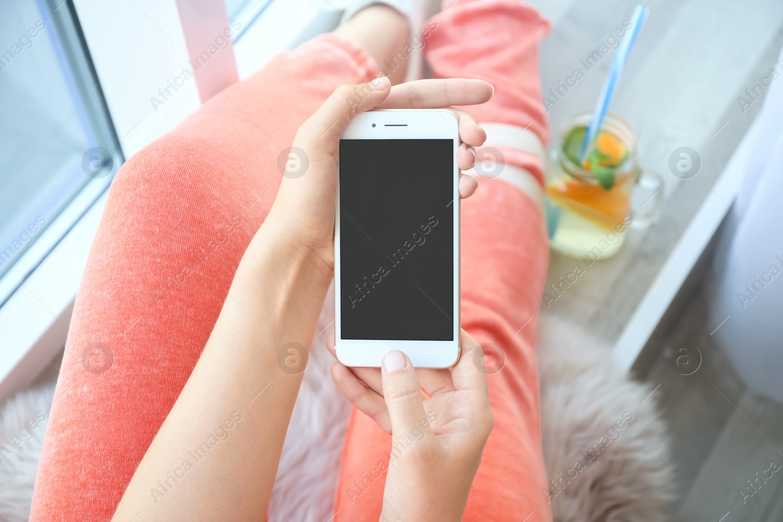 Photo of Young woman holding mobile phone with blank screen in hands indoors