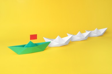 Photo of Group of paper boats following green one on yellow background,. Leadership concept
