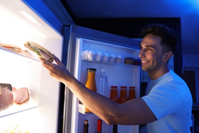 Photo of Man taking sandwich out of refrigerator in kitchen at night