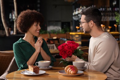 Photo of International dating. Handsome man presenting roses to his girlfriend in restaurant