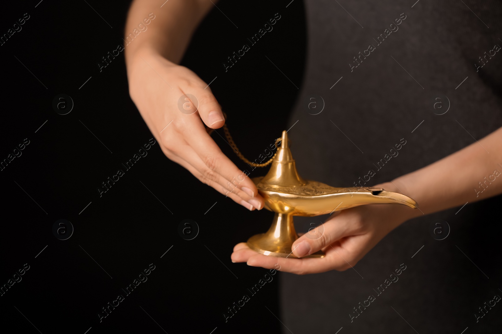 Photo of Woman rubbing magical Aladdin lamp on black background, closeup