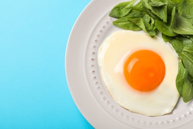 Photo of Plate of fried egg and spinach on light blue background, top view with space for text. Healthy breakfast
