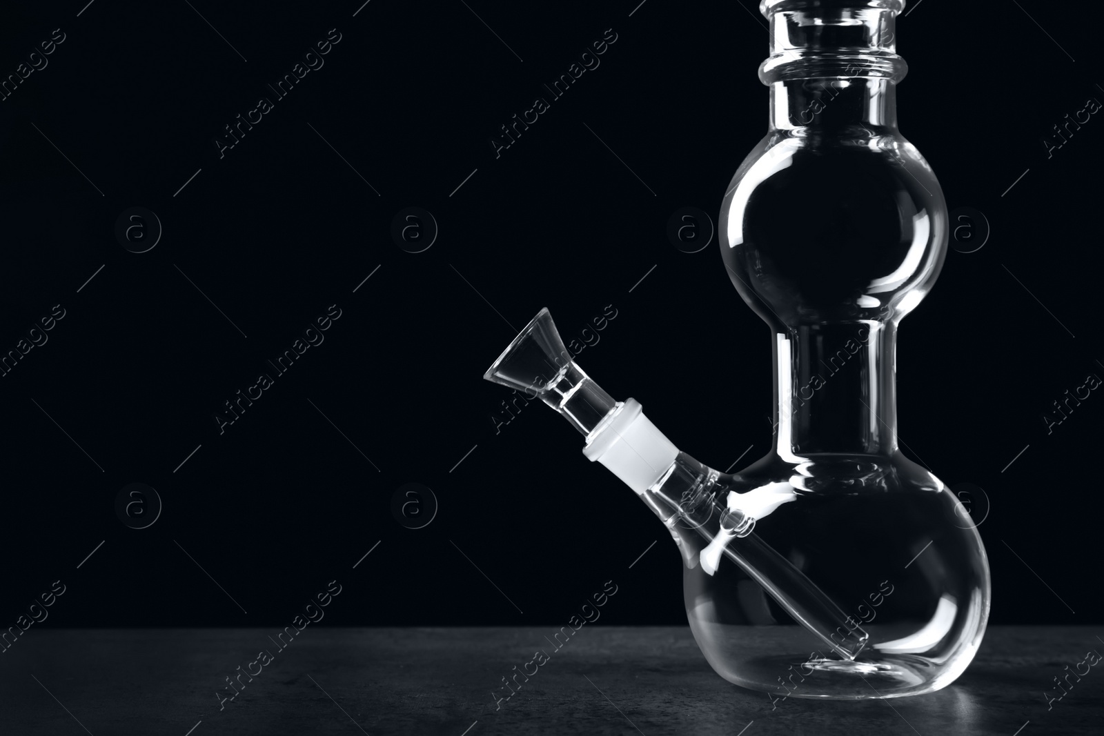 Photo of Glass bong on grey table against black background, space for text. Smoking device