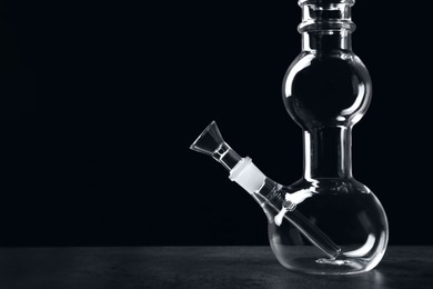 Glass bong on grey table against black background, space for text. Smoking device