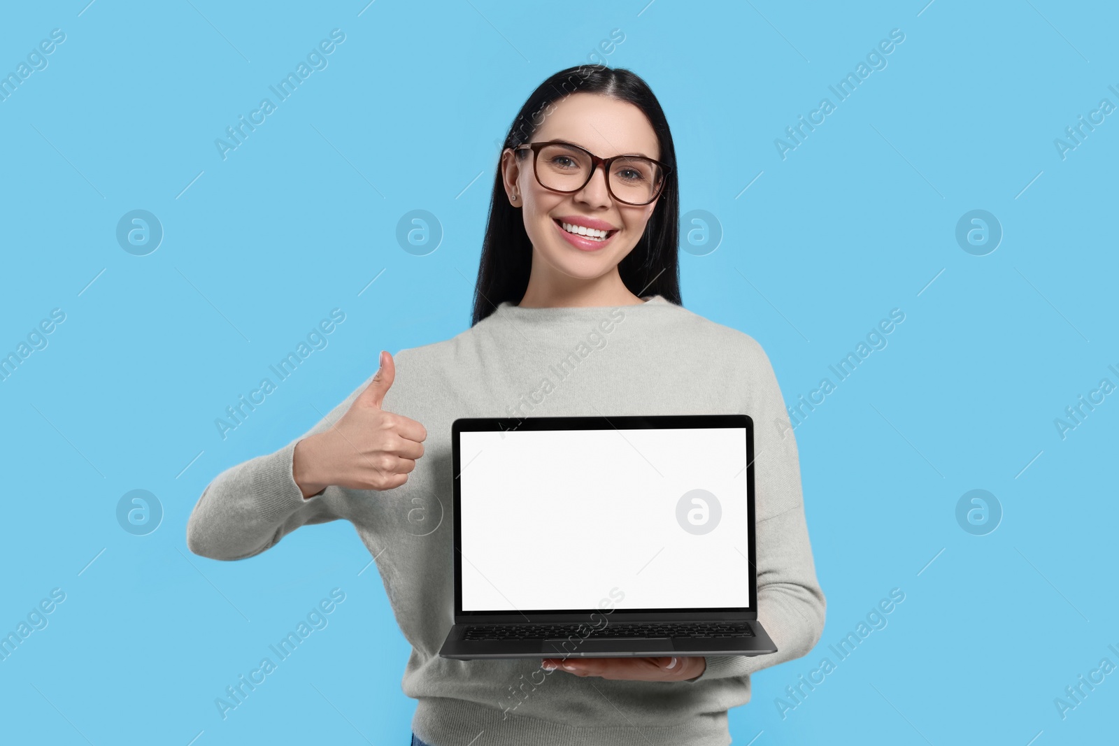 Photo of Happy woman with laptop showing thumb up on light blue background