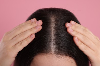 Woman examining her hair and scalp on pink background, closeup