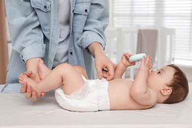 Mother changing baby's diaper on bed at home, closeup