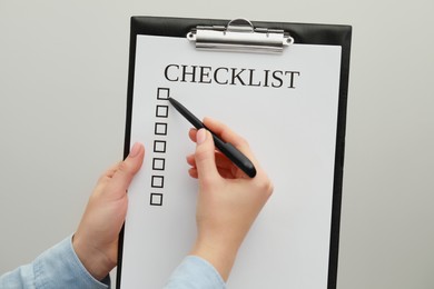 Woman filling Checklist on light grey background, closeup