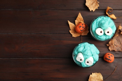 Photo of Delicious desserts decorated as monsters on wooden table, flat lay with space for text. Halloween treat