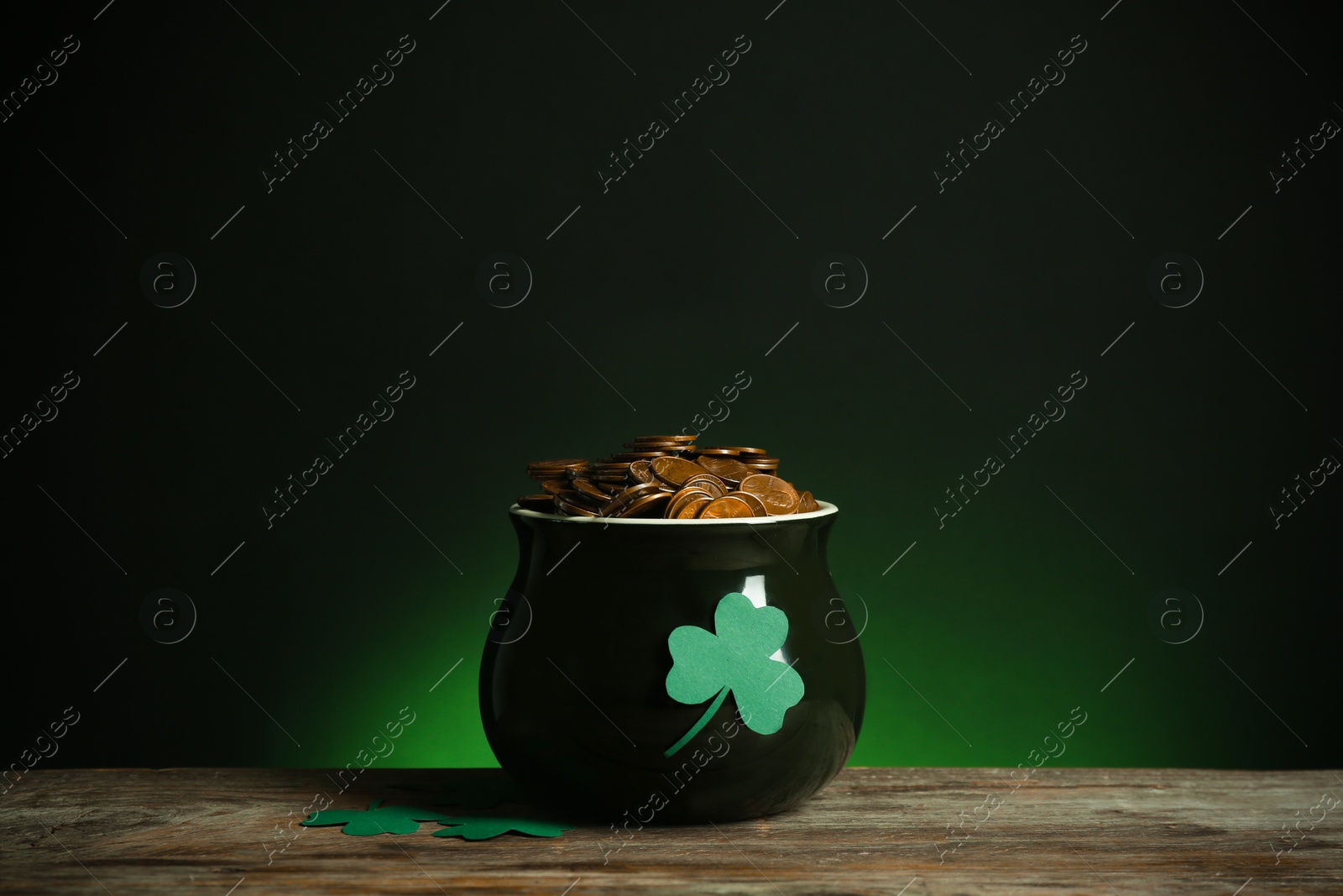 Photo of Pot with gold coins and clover on wooden table against dark background. St. Patrick's Day