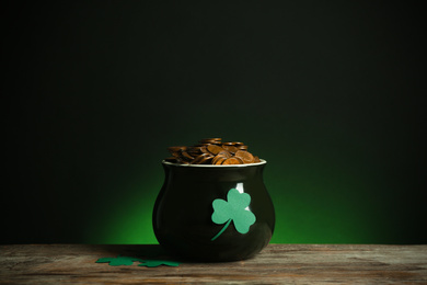 Photo of Pot with gold coins and clover on wooden table against dark background. St. Patrick's Day