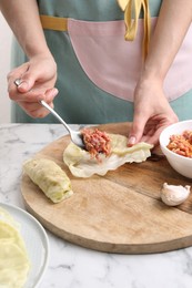 Woman preparing stuffed cabbage roll at white marble table, closeup