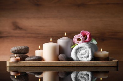 Photo of Beautiful composition with spa stones, flowers and burning candles on mirror table against wooden background