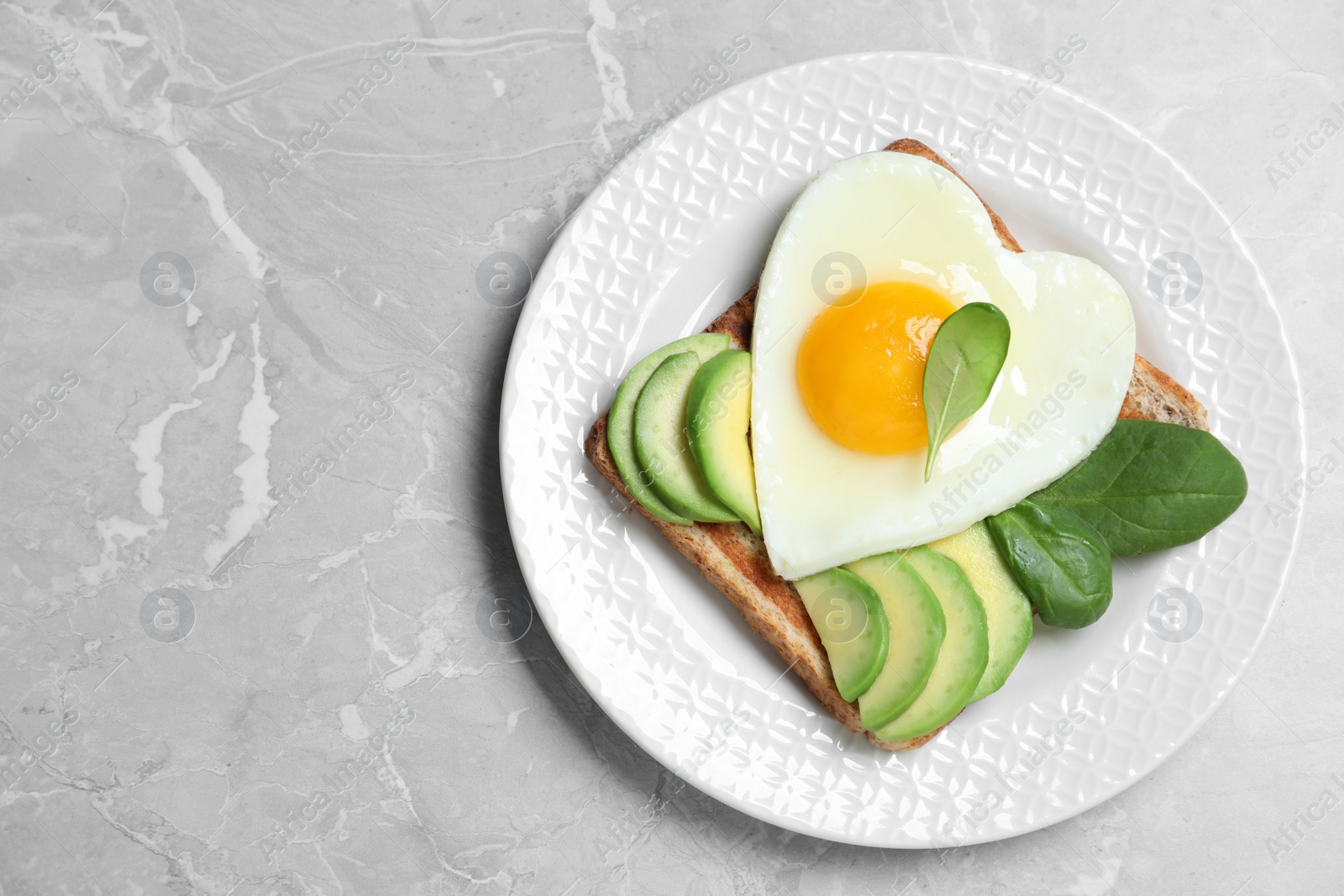 Photo of Tasty breakfast with heart shaped fried egg on grey table, top view