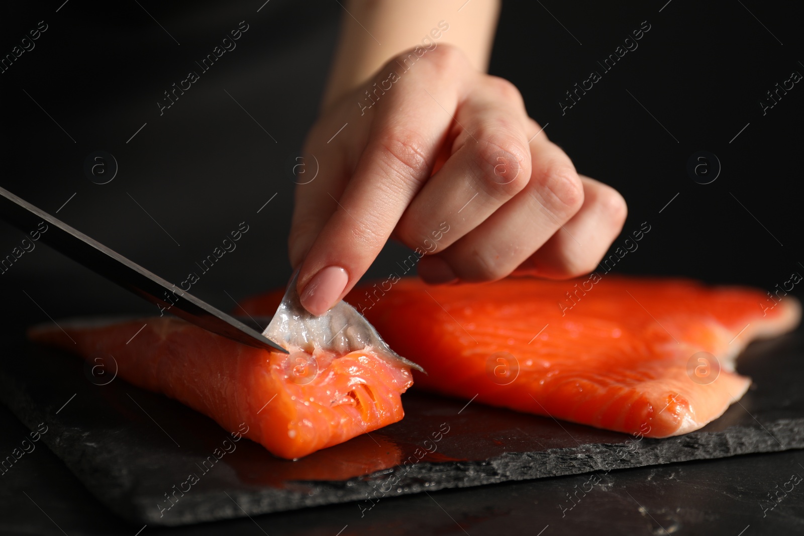 Photo of Chef removing scales from salmon for sushi at dark table, closeup