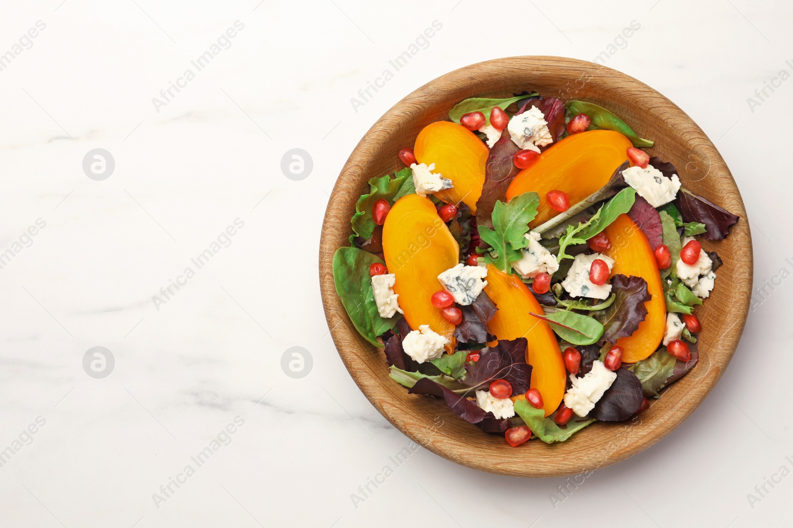 Photo of Delicious persimmon salad with cheese and pomegranate served on white marble table, top view. Space for text