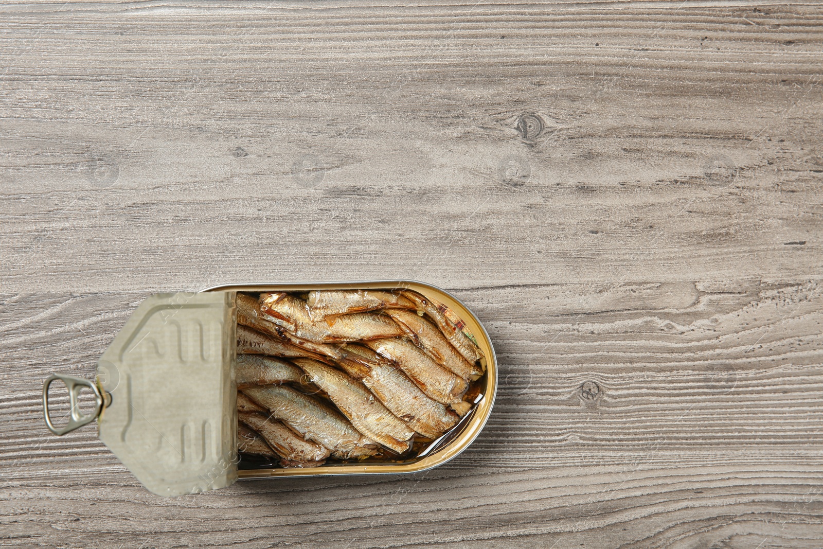 Photo of Open tin can of sprats on wooden background, top view