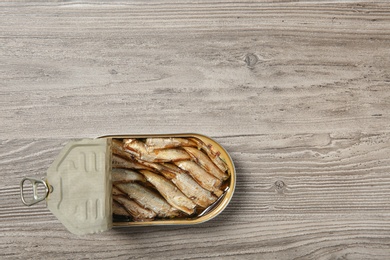 Photo of Open tin can of sprats on wooden background, top view