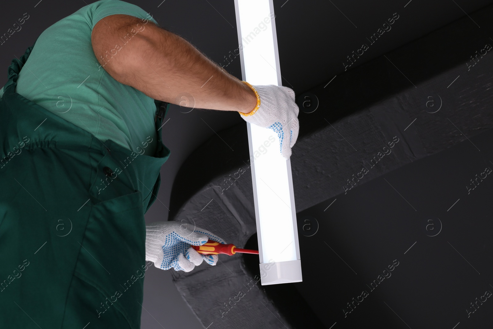 Photo of Ceiling light. Electrician installing led linear lamp indoors, bottom view