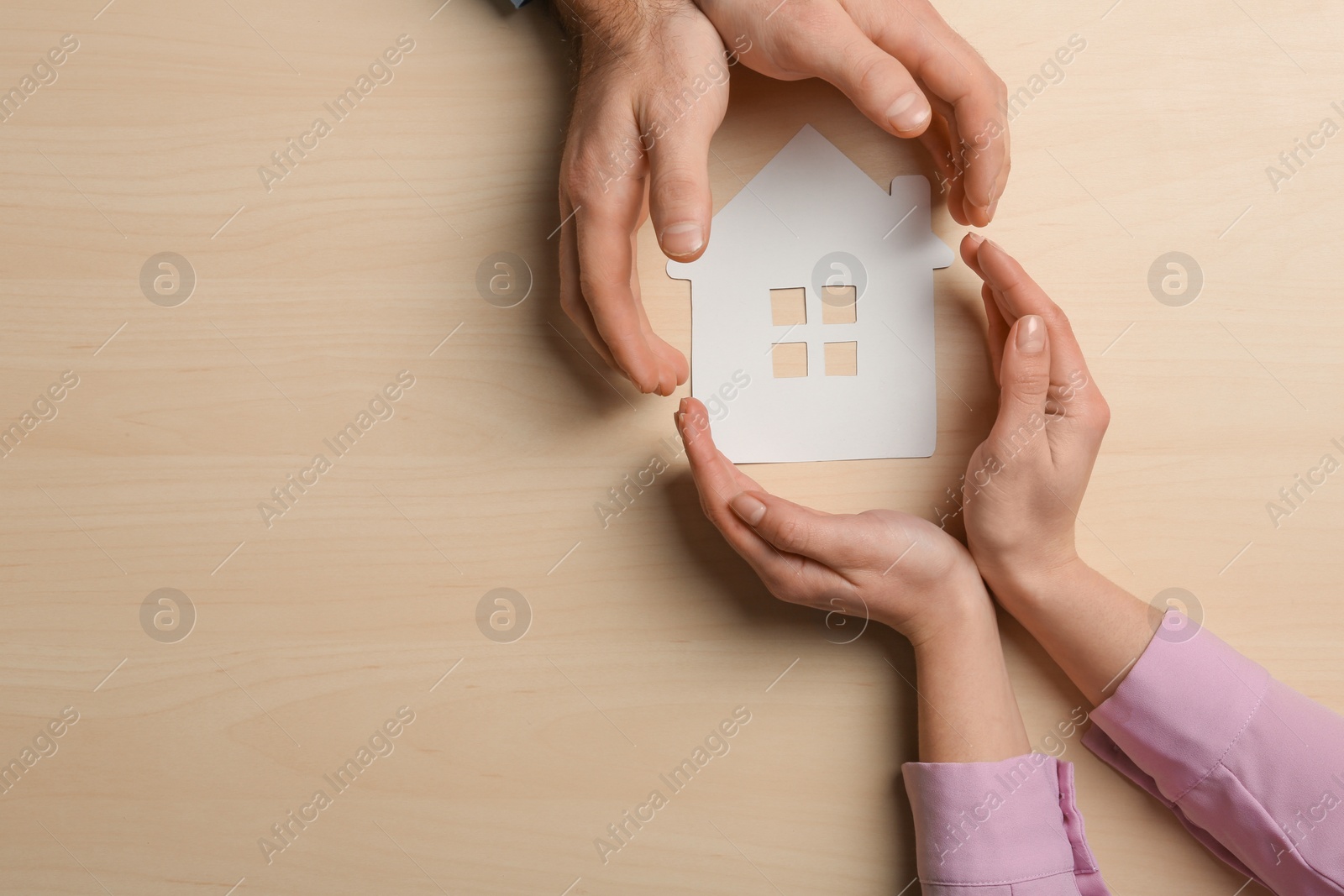 Photo of Couple holding hands near paper silhouette of house on wooden background, top view with space for text. Home insurance