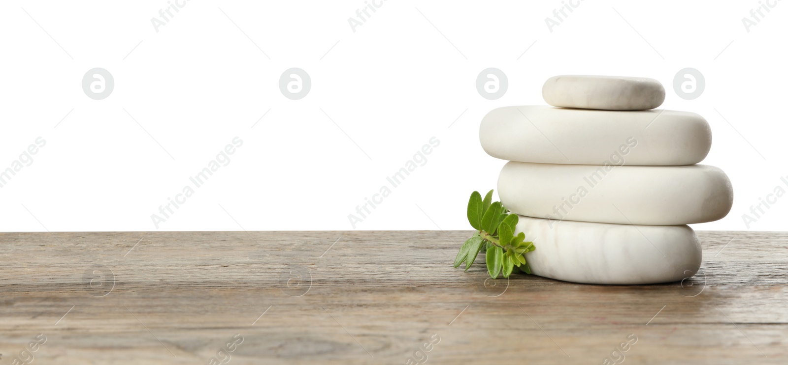 Photo of Stack of spa stones and green branch on wooden table against white background. Space for text