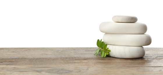 Photo of Stack of spa stones and green branch on wooden table against white background. Space for text