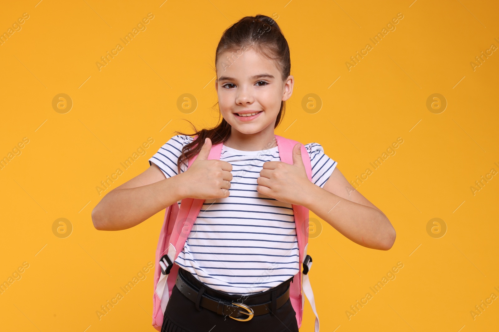 Photo of Cute schoolgirl showing thumbs up on orange background