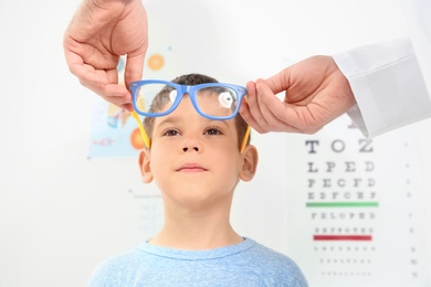 Photo of Male ophthalmologist putting glasses on  little boy in clinic
