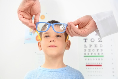 Male ophthalmologist putting glasses on  little boy in clinic