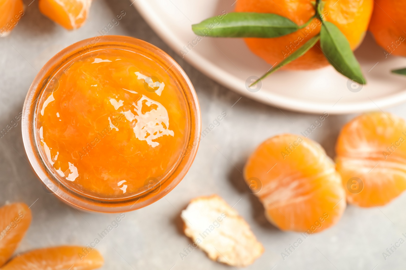 Photo of Tasty jam and fresh tangerines on light grey table, flat lay. Space for text