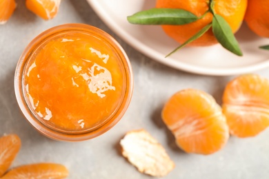 Photo of Tasty jam and fresh tangerines on light grey table, flat lay. Space for text