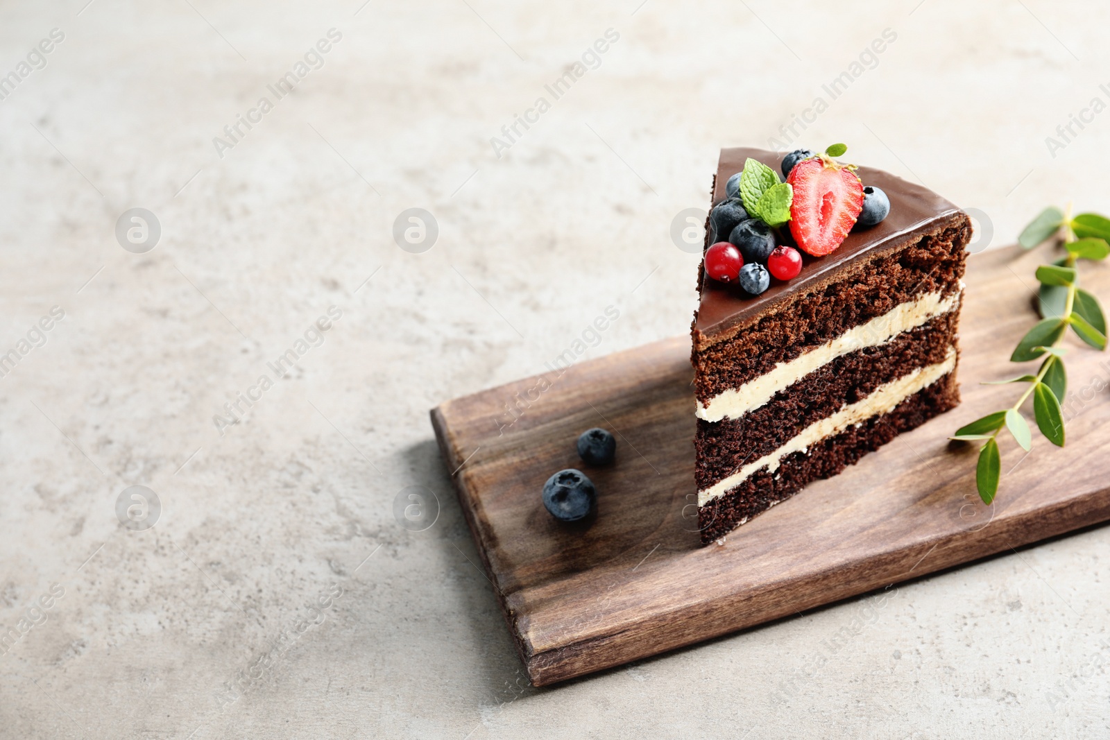 Photo of Wooden board with slice of chocolate sponge berry cake on grey background