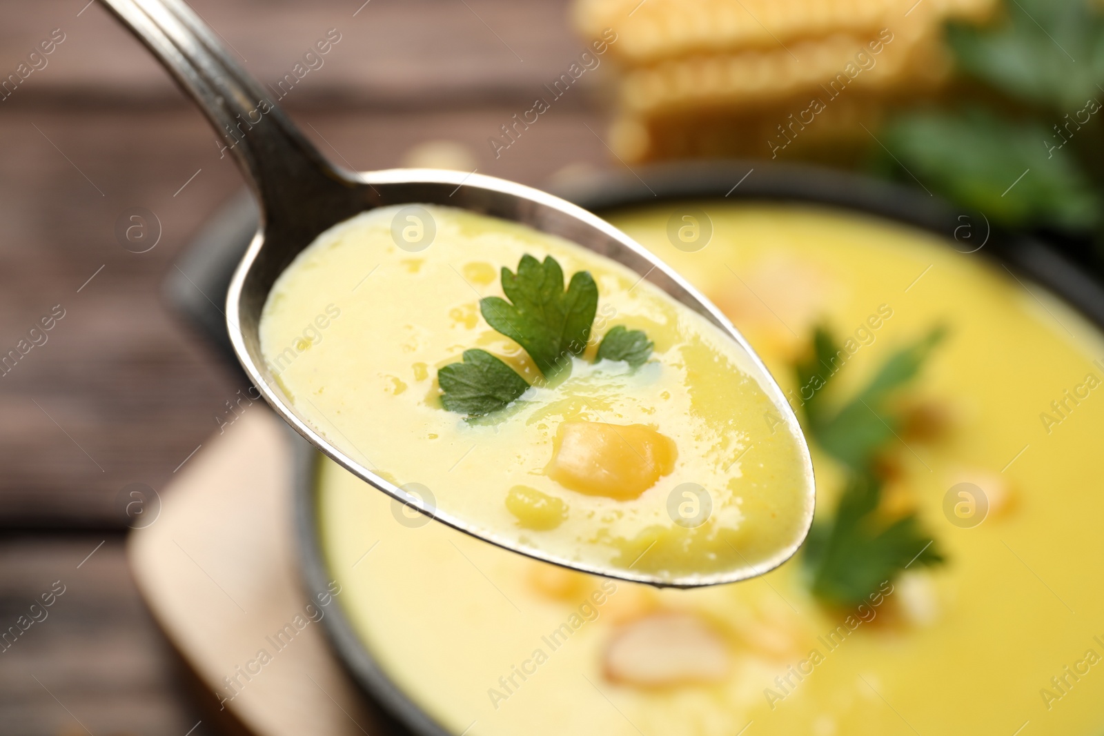 Photo of Spoon of delicious corn soup over full pot, closeup