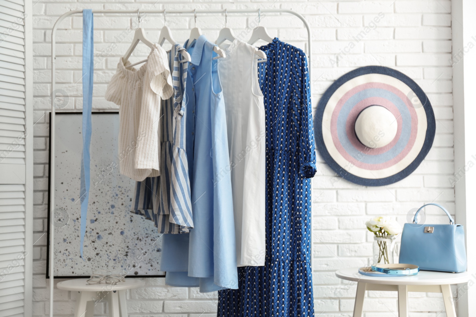 Photo of Wardrobe rack with women's clothes at white brick wall in room