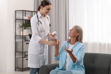 Photo of Young healthcare worker giving bottle of pills and water to senior woman indoors