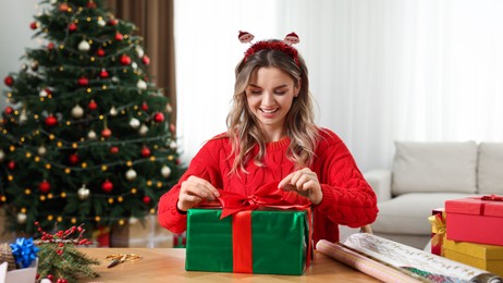 Photo of Beautiful young woman wrapping Christmas gift at home