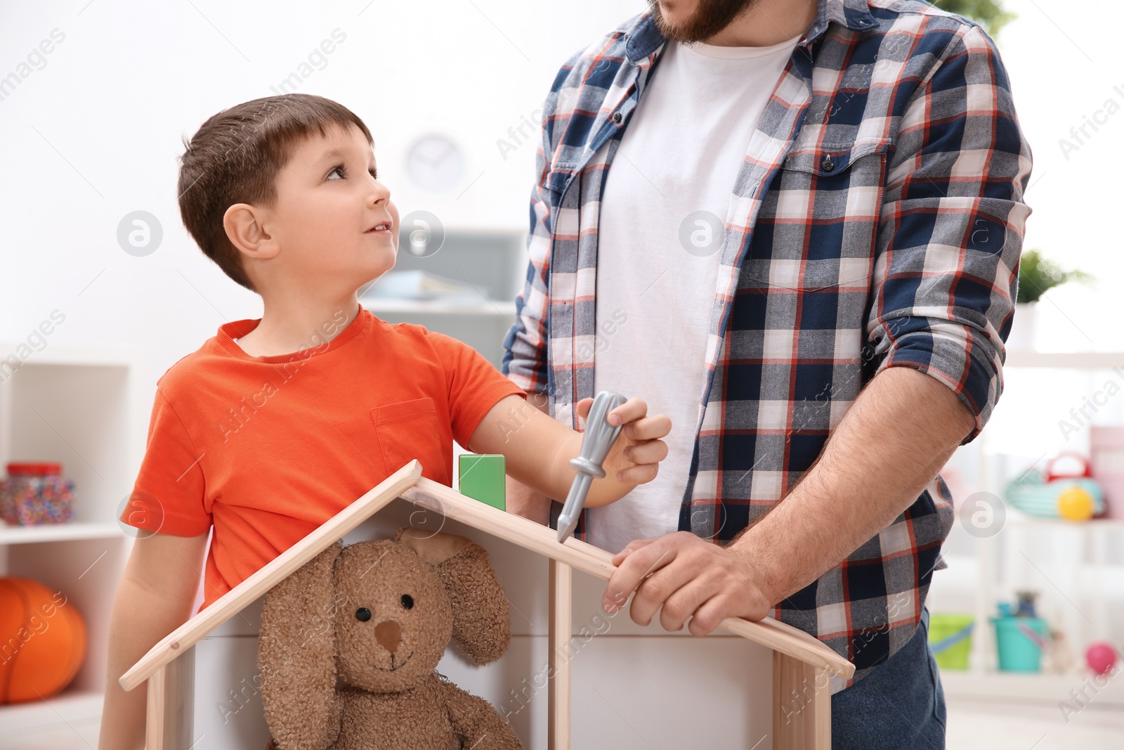 Photo of Man and his child playing builders with wooden doll house at home