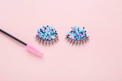 Photo of False eyelashes, sequins and mascara brush on pink background, flat lay